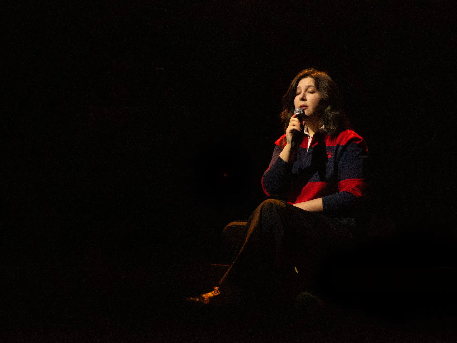 Lucy Dacus sitting on stage, singing.
